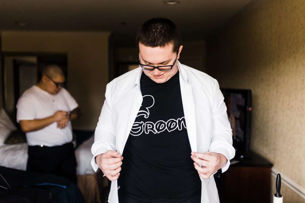 Groom pulls white shirt over black disney shirt