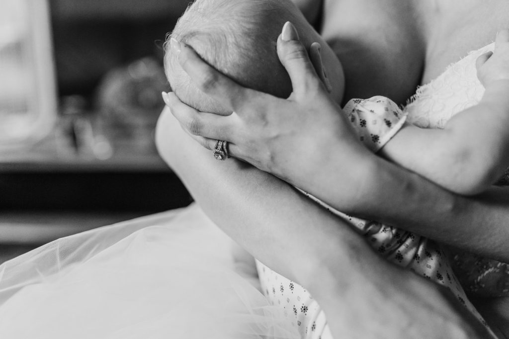 Bride supports babies head with wedding ring hand