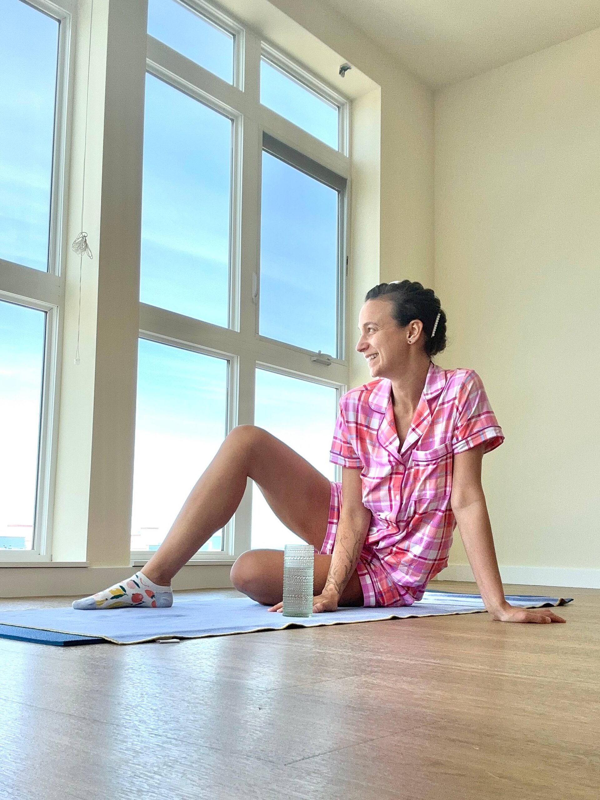 Jaclynn looks out large city windows in new apartment in pink plaid pajamas.